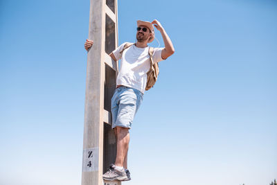 Full length of man standing on ladder against clear sky during sunny day