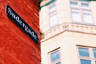 Low angle view of road sign on red wall in city