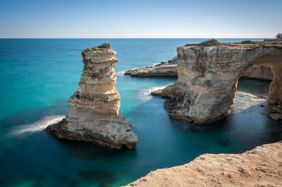 Rock formations in sea against clear blue sky