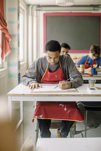 Male teenage student doing artwork during painting class at high school