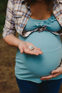 Midsection of pregnant woman holding seashell while standing outdoors