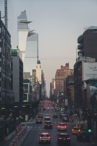 Traffic on city street by buildings against sky at dusk