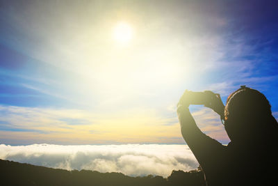 Silhouette person holding sun against sky during sunset