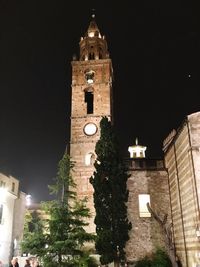 Low angle view of clock tower amidst buildings at night