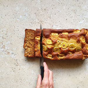 Close up of hand slicing loaf of bread on stone table