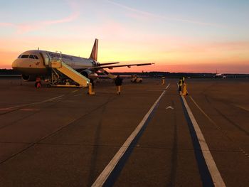 Airplane on airport runway against sky during sunset