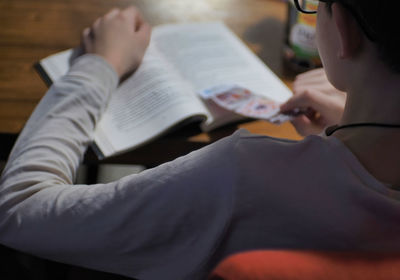Midsection of teen reading book at home