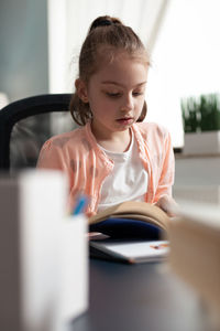 Girl reading book while sitting at home