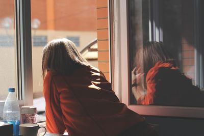 Rear view of woman looking through window at home