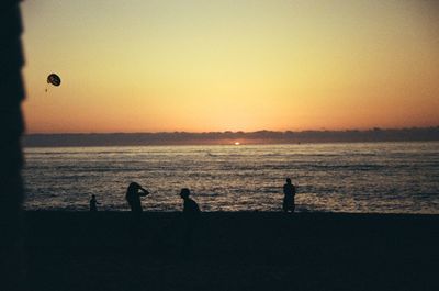 Silhouette people on beach against clear sky during sunset