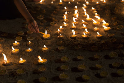 Midsection of person with illuminated burning candles in temple