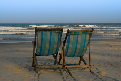 Deck chairs on beach against sky