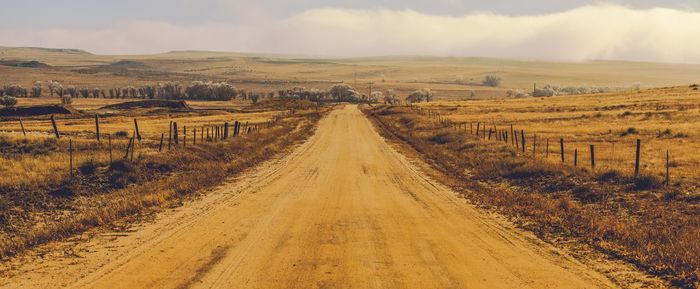 Dirt road amidst field against sky