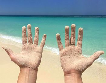 Close-up of hands on sea against sky