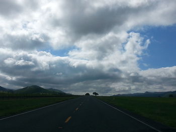 Empty road on field against cloudy sky