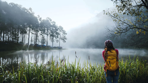 Rear view of woman standing by lake against trees