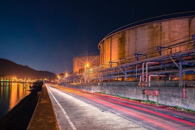Light trails on road by industry at night