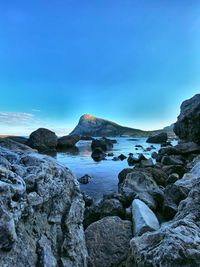 Rocks by sea against blue sky