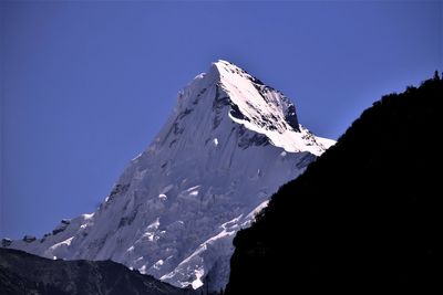 Low angle view of snowcapped mountains against clear blue sky