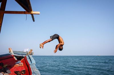 Man jumping from boat into sea against clear sky