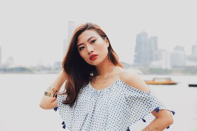 Portrait of young woman standing against river in city