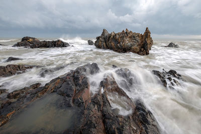 Long exposure image of waves crashing at beach against storm clouds