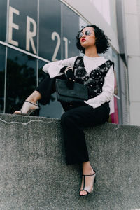 Full length of woman sitting on retaining wall in city