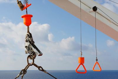 Low angle view of boat equipment hanging by sea against sky