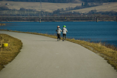 Rear view of friends inline skating by lake on road