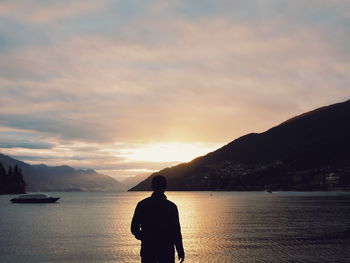 Rear view of man against lake during sunset