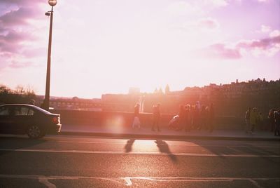 Vehicles on road against sky during sunset