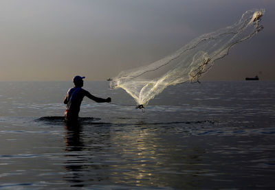 Full length of man fishing in sea against sky