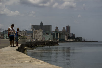 Man standing on sea by buildings against sky