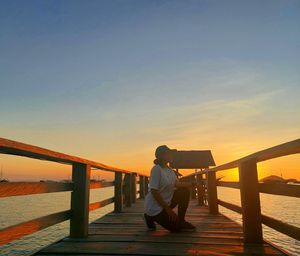 Man sitting on railing against sky during sunset