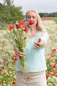 Beautiful middle-aged blonde woman stands among a flowering field of poppies