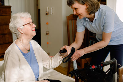 Smiling female healthcare worker looking at senior woman sitting with rollator in bedroom at nursing home