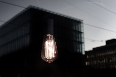 Low angle view of illuminated light bulb hanging on building