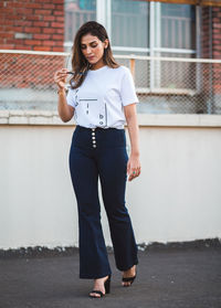 Full length portrait of young woman standing against building