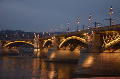 Illuminated bridge over river against sky in city at night