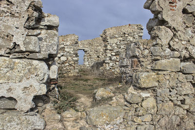 Stone wall by rocks against sky