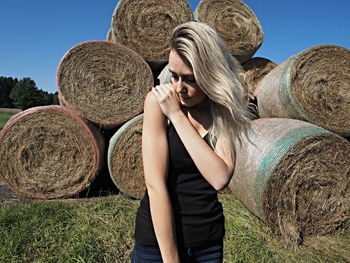 Young woman standing against hay bales on field during sunny day