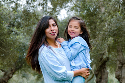 Portrait of mother carrying daughter against tree in forest