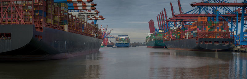 Boats in canal by harbor against sky