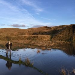 Person standing in shallow water by hill against sky