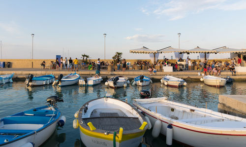 Boats moored on sea against people