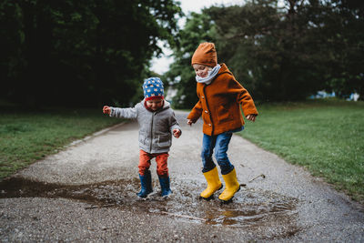 Two boys jumping in the puddles at the park on cloudy day