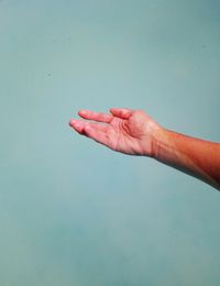 Close-up of hand gesturing against turquoise background