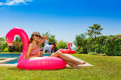 Side view of woman sitting on grassy field against clear blue sky