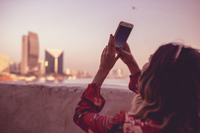 Close-up of young woman taking picture on mobile phone against sky