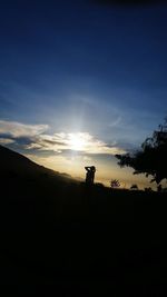 Silhouette man photographing on landscape against sky during sunset